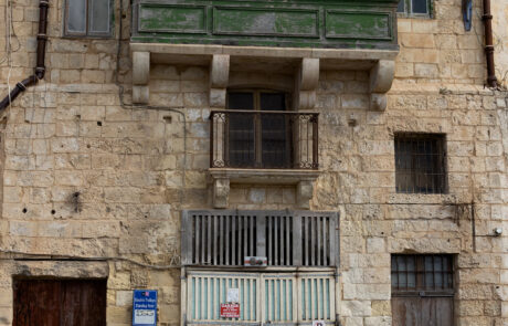 Historic limestone building with a green shuttered balcony in Mdina