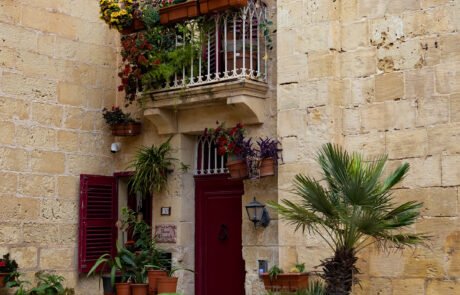 Narrow street with colorful shuttered balconies and potted plants in Mdina