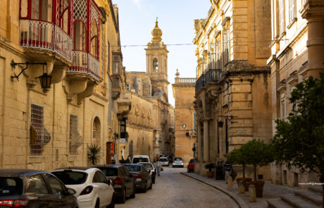 Street lined with historic limestone buildings and red Maltese balconies in Mdina