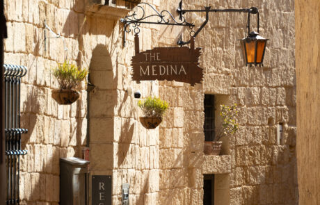 Balconied limestone street lined with hanging plants in Mdina
