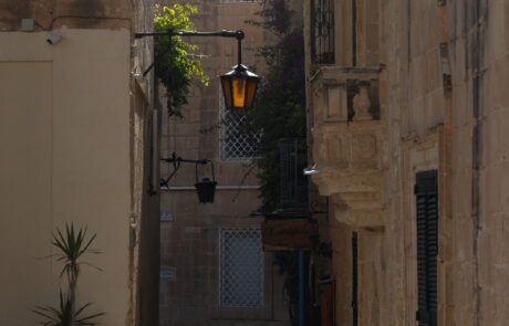 Narrow lamplit alley between historic stone buildings in Mdina, Malta