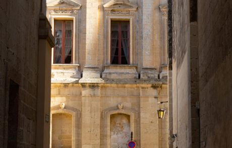 Historic stone street with pedestrians walking past a baroque building in Mdina, Malta