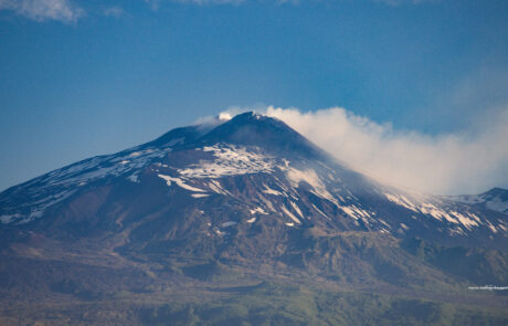 Snow-capped Mount Etna volcano with a rugged rocky foreground