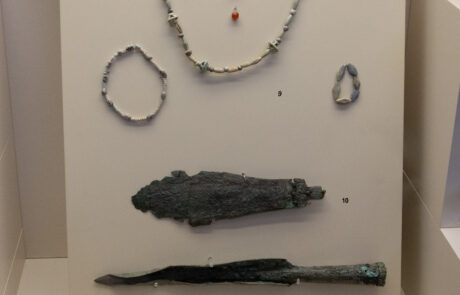 Ancient jewelry and small vessels displayed in a glass case at the Olympia Archaeological Museum