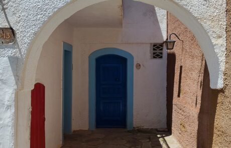 Whitewashed stone archway with a blue door in an Arolithos village alley