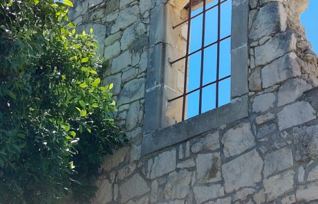 Ruined stone wall with an arched, barred window at Arolithos traditional Cretan village