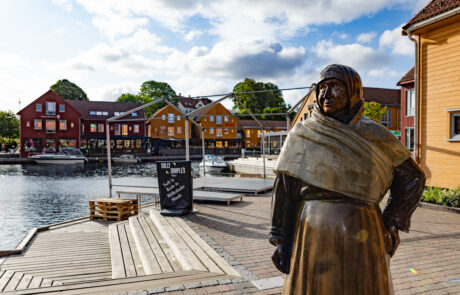 Wooden statue on the waterfront promenade with colorful houses behind it, Kristiansand, Norway