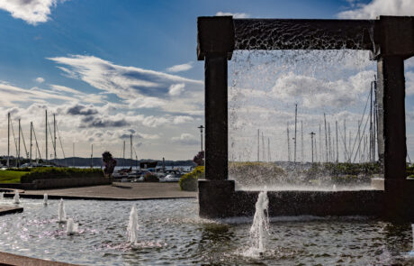 Fountain sculpture spraying water at a marina with sailboats, Kristiansand, Norway