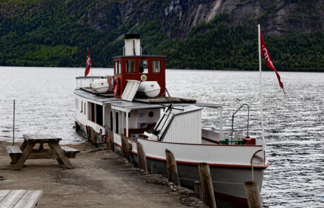 Old paddle steamer docked with Norwegian flags against a fjord backdrop