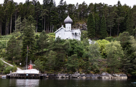 Small white chapel on a rocky point in the fjord with a boat docked nearby