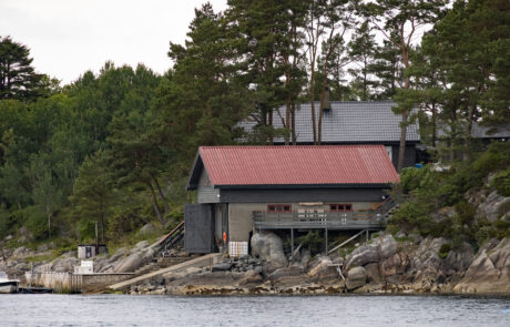 Waterfront house with a red roof on a rocky, forested shoreline