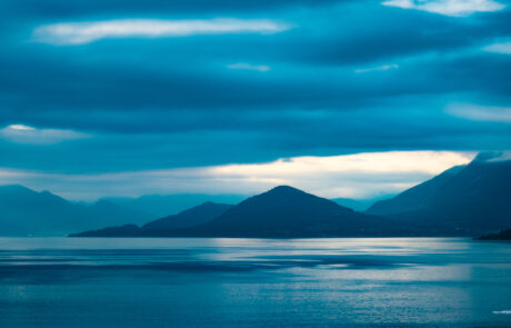 Calm blue fjord panorama with mountain silhouettes and streaky clouds