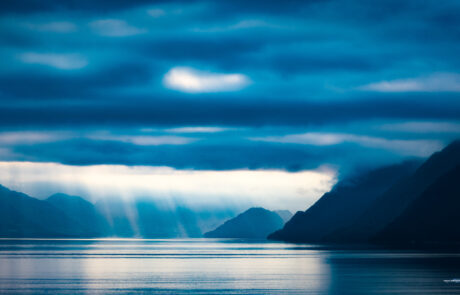 Dramatic sun rays breaking through clouds over the blue fjord water