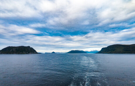 Wide fjord view with islands and a boat wake under a cloudy sky