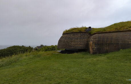 Grass-covered WWII bunker on a hill under an overcast sky