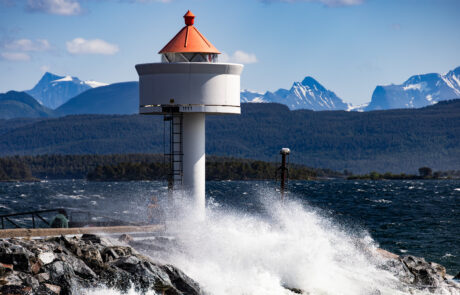Lighthouse on a breakwater with crashing waves and snow-capped mountains, Molde, Norway