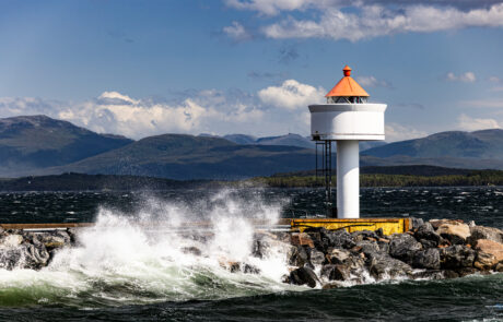 Lighthouse on a breakwater with waves crashing against it, mountains in the background, Molde, Norway