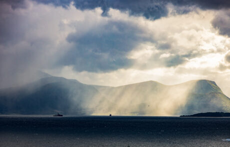 Mountain silhouette with dramatic sun rays breaking through clouds over the fjord