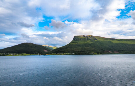 Green mountain peak across calm fjord water under a blue sky, Molde, Norway