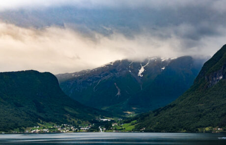 Village nestled in a fjord valley surrounded by mountains and clouds, Flam, Norway