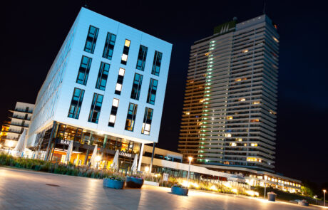 The AJA Maritim hotel building illuminated in blue at night with palm trees in front