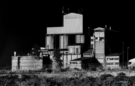 Black-and-white photo of an abandoned industrial factory building with tanks and a chimney