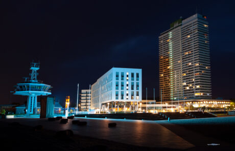 3D architectural image of the AJA Maritim hotel complex illuminated at night with a lighthouse tower and fountain