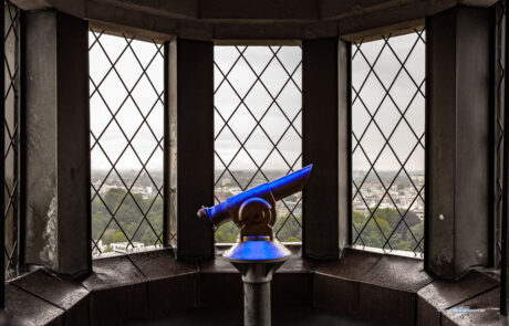 View through a church tower arched window with a telescope overlooking Luebeck rooftops