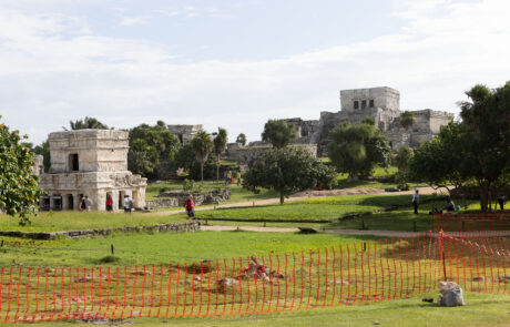 El Castillo pyramid at Tulum behind an orange safety fence with visitors on the grass