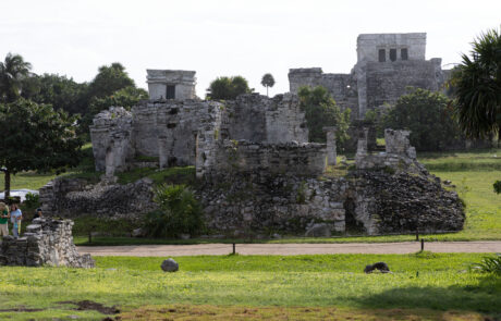 Mayan pyramid temple surrounded by grass and trees with visitors nearby, Tulum