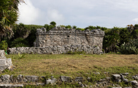 Mayan pyramid temple surrounded by grass and trees with visitors nearby, Tulum