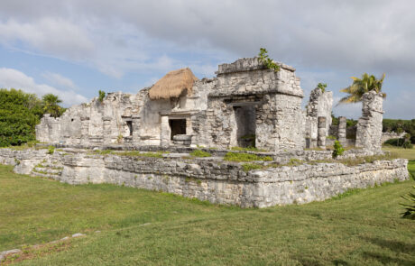 Mayan ruins on a cliff above turquoise Caribbean water with palm trees, Tulum